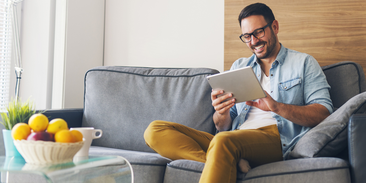 Man on a couch using CenturyLink fiber internet to surf the web on his tablet.