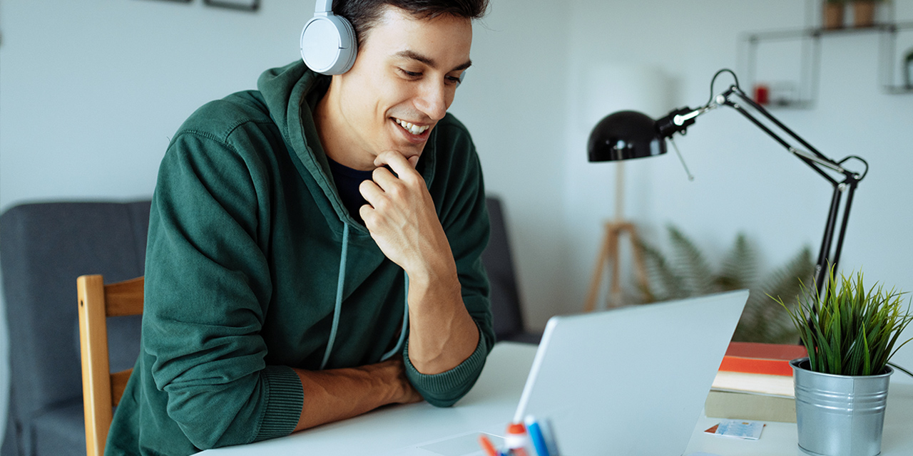 Man sitting at desk wearing headphones looking at laptop