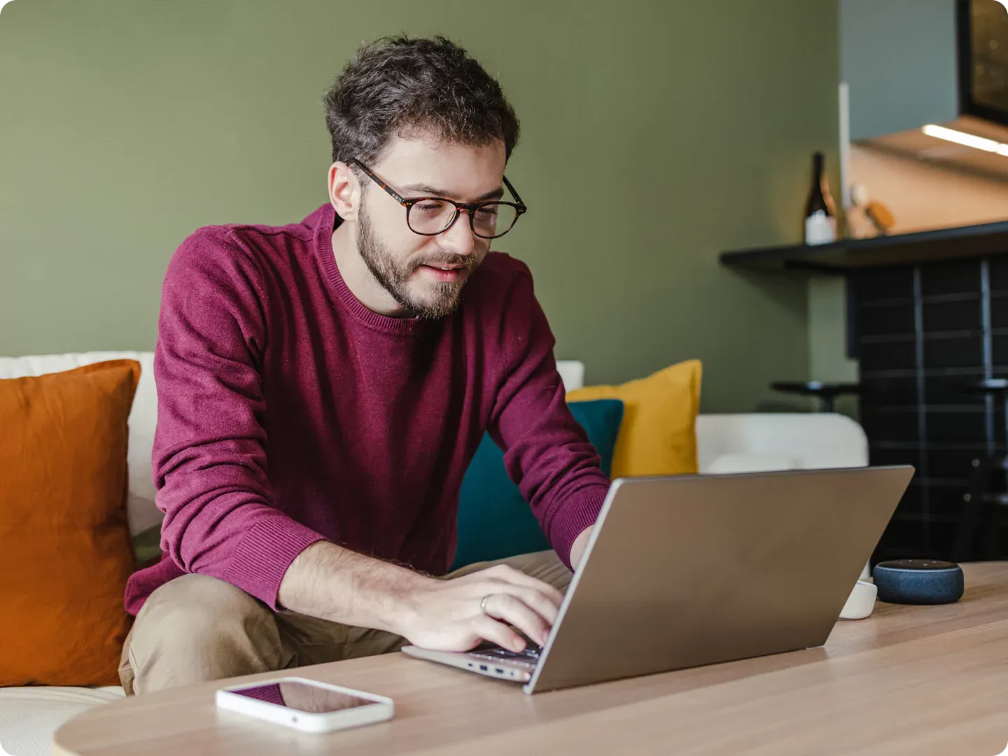 Man wearing magenta sweater works on laptop with fast internet at home.