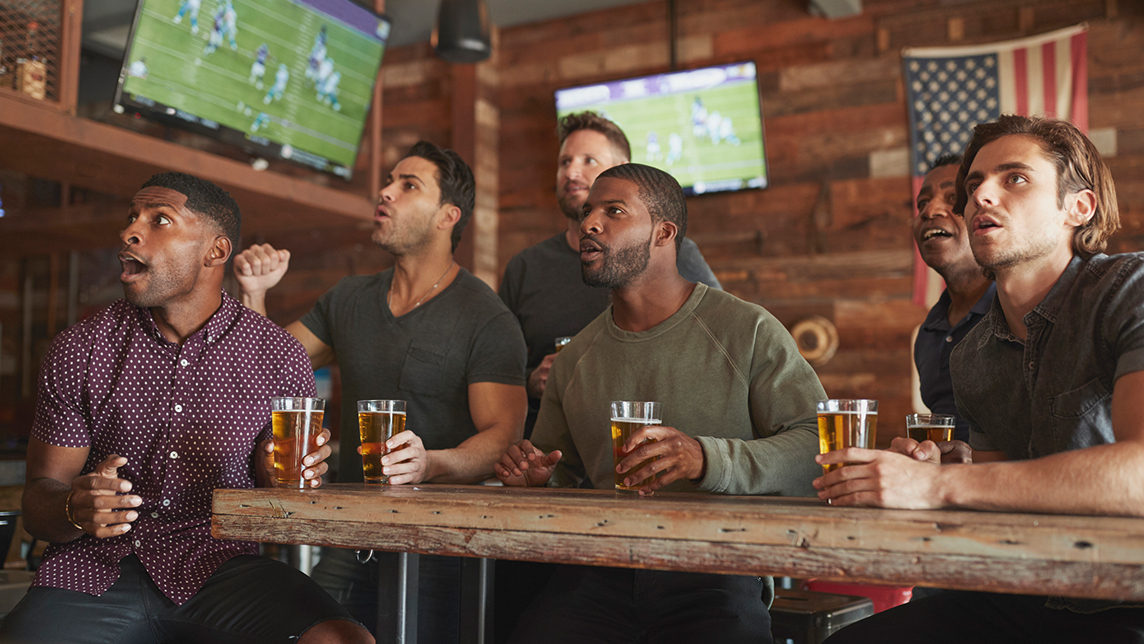 A group of men drink while watching football.