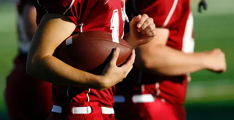 Closeup of college football players holding football.