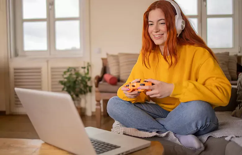 Woman wearing yellow plays video games at home on her laptop.