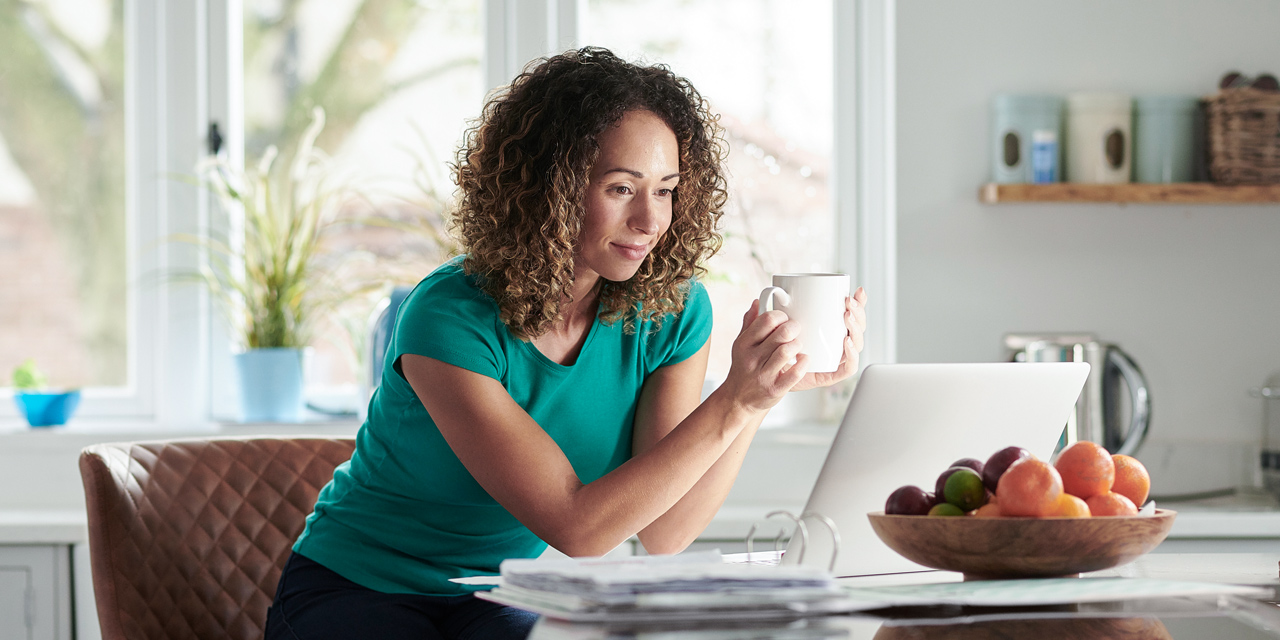 woman at kitchen counter drinking coffee using CenturyLink internet to check her email