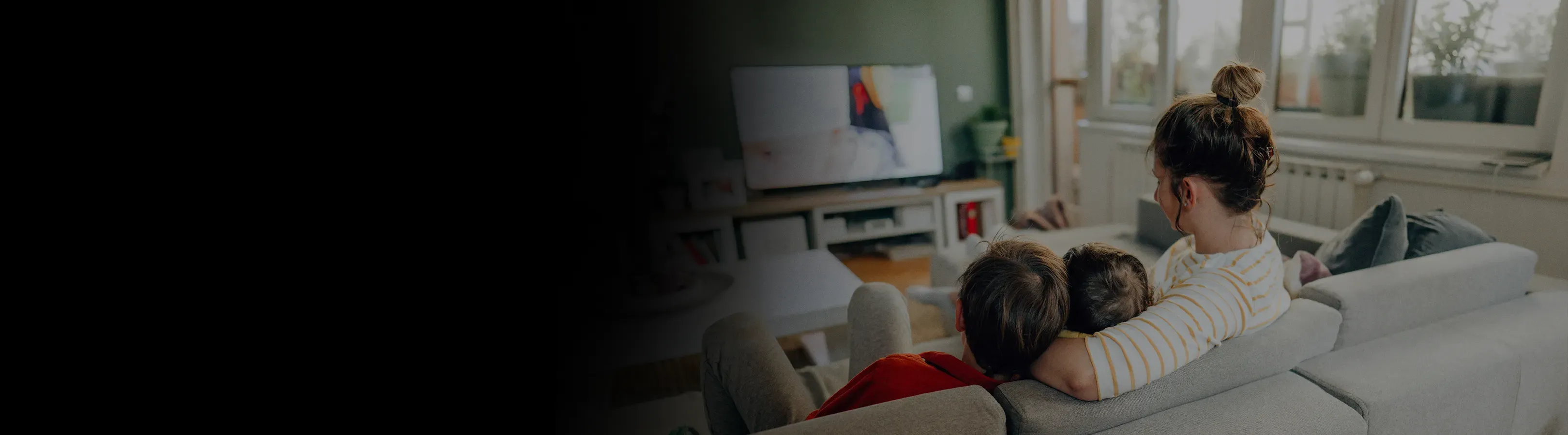A mother cuddles two children on a sofa while they watch television together.