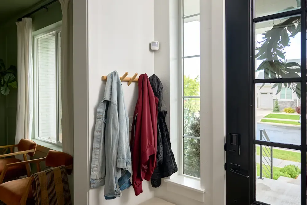 A small white motion sensor mounted on a wall above a wooden coat rack in a modern home entryway.