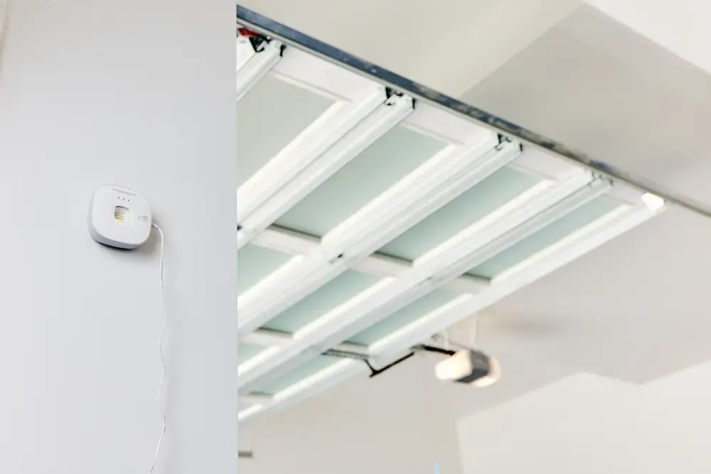 A white myQ smart garage hub mounted on a wall next to an open sectional garage door.