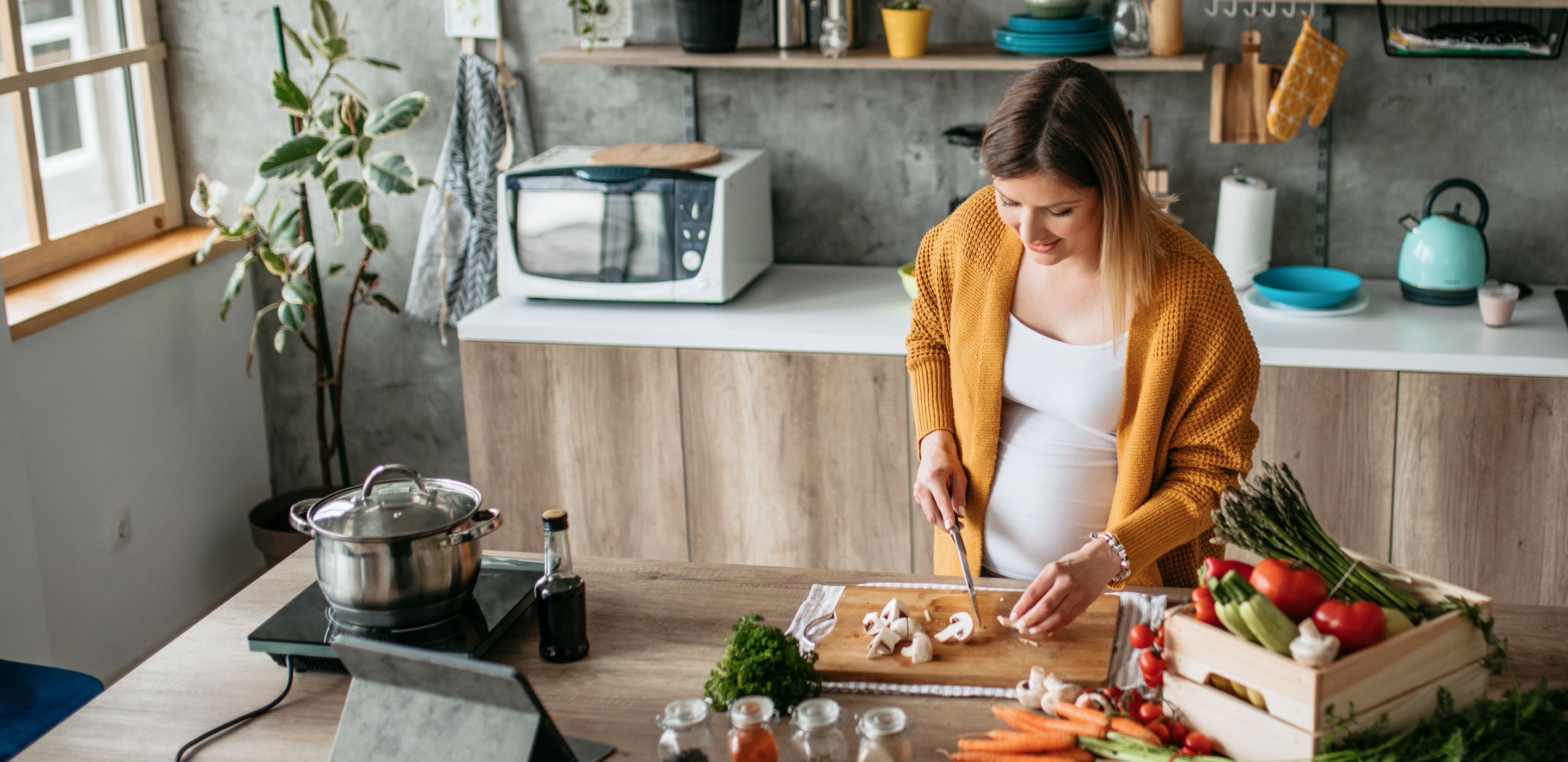 Pregnant woman cooking in the kitchen with tablet.