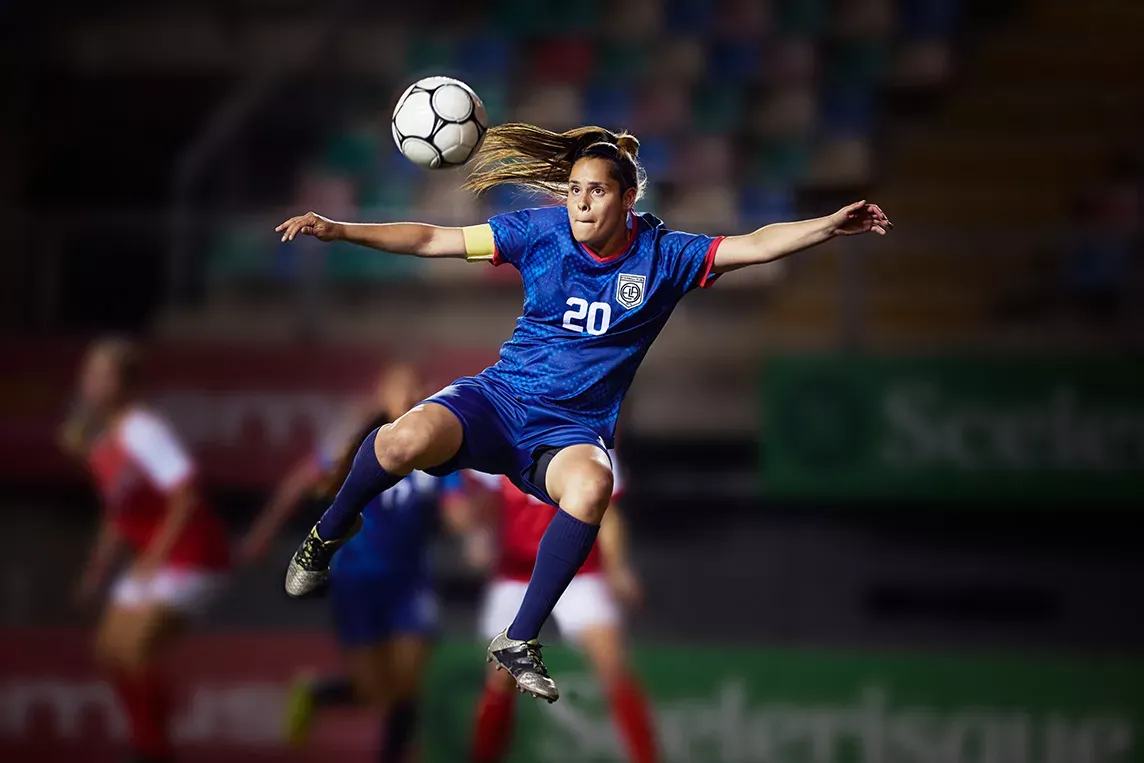 Professional woman playing soccer kicks ball in the air