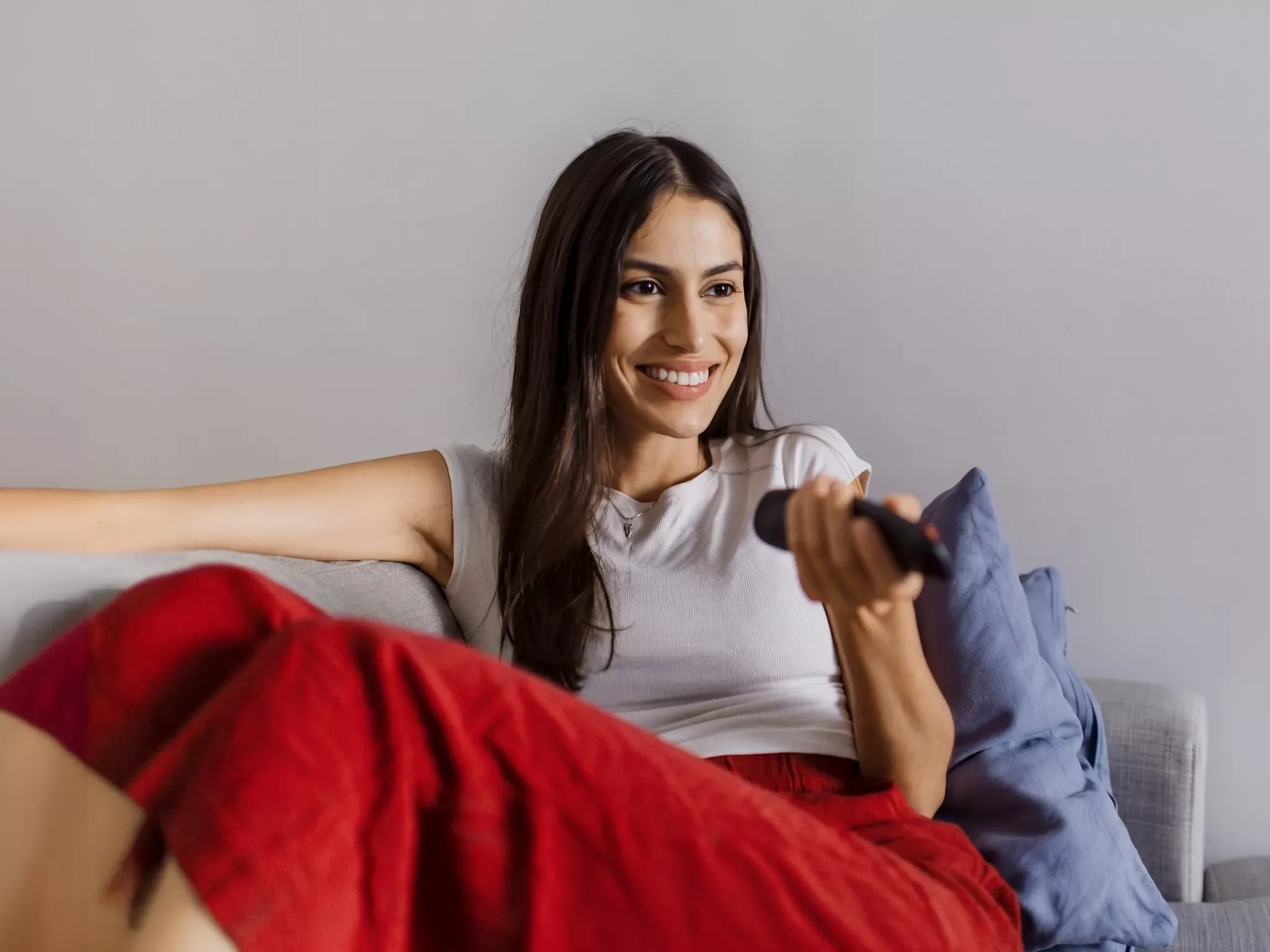 Woman in Bright Red Pants smiling and watching tv, while reclining on the couch.