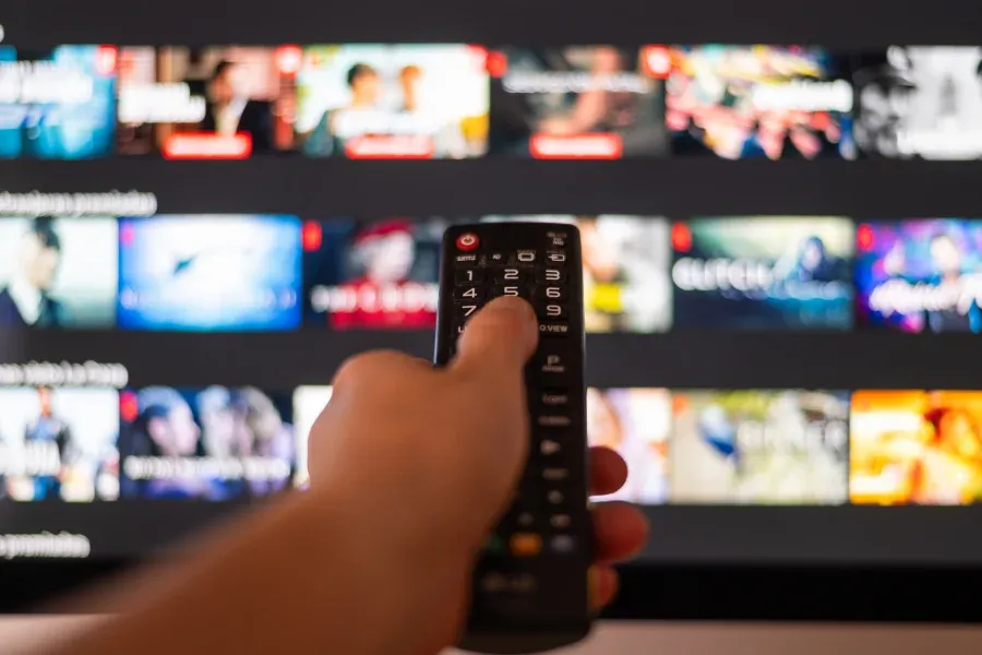 A hand points a remote at a TV screen full of streaming show thumbnails.