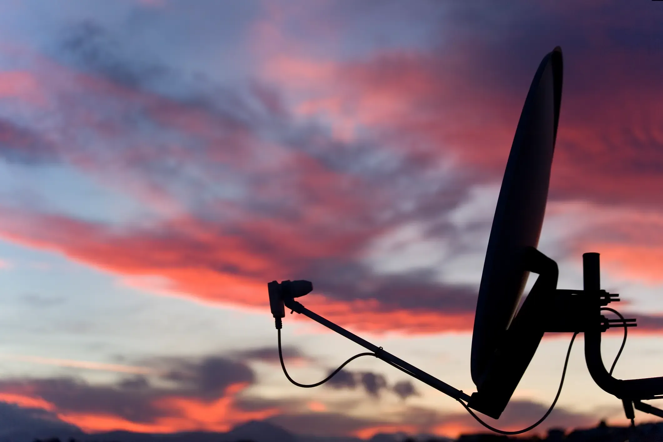 Silhouette of a satellite dish against a vibrant sunset sky with streaks of pink and purple clouds.