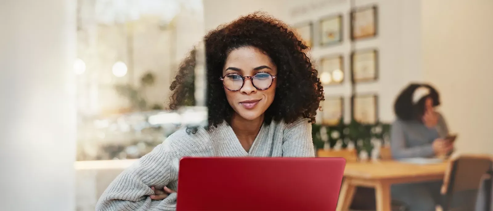 A small business woman uses her red laptop and subtly smiles as she is working.