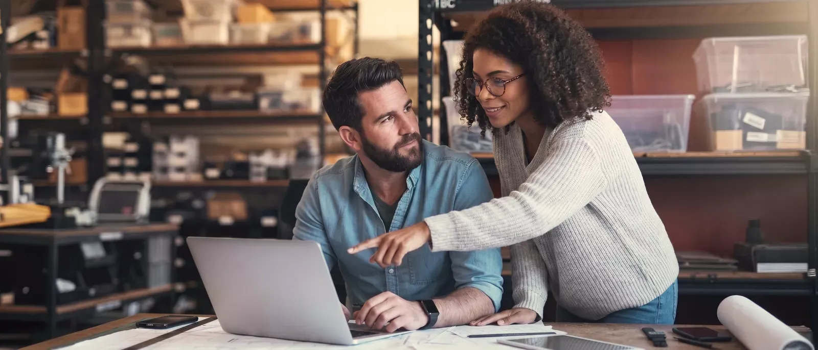 A small businss woman smiles and looks over her business partners shoulder as they talk about how great their new internet is.