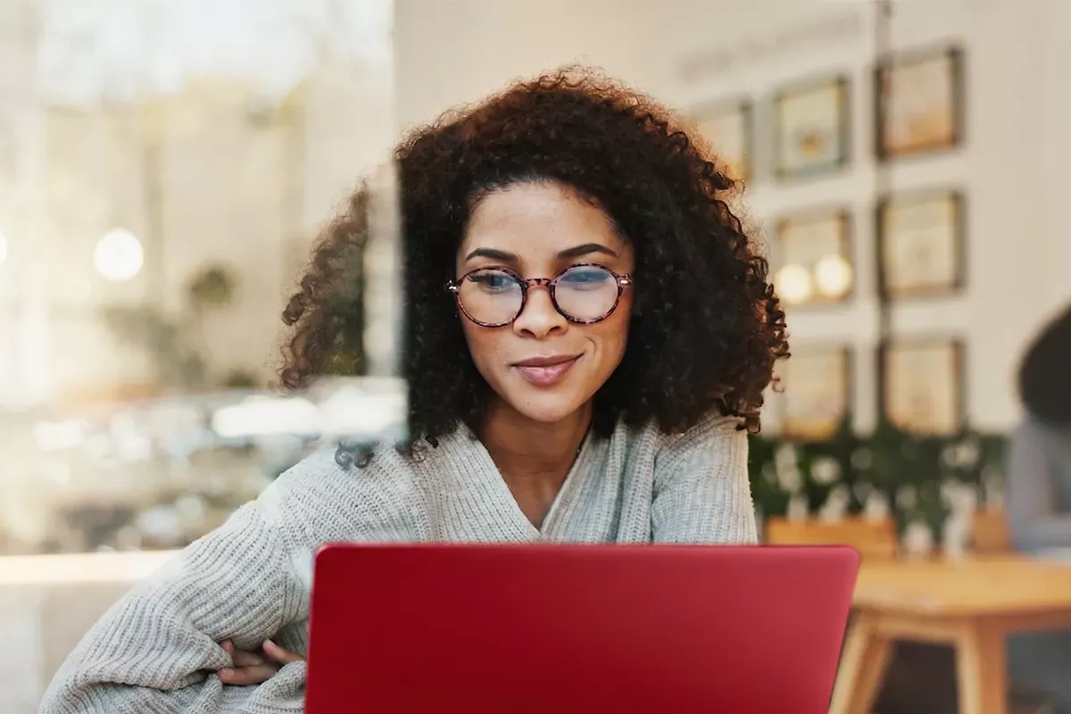A small business woman uses her red laptop and subtly smiles as she is working.