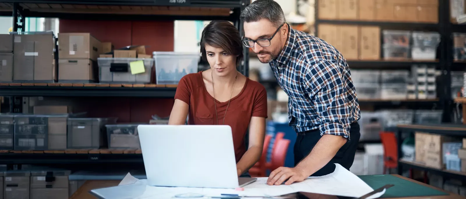 Two people working on a laptop, they are in a small business office/warehouse space.