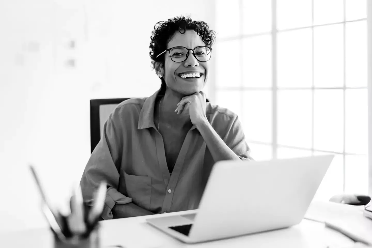 Smiling woman with glasses sitting at a desk with a laptop