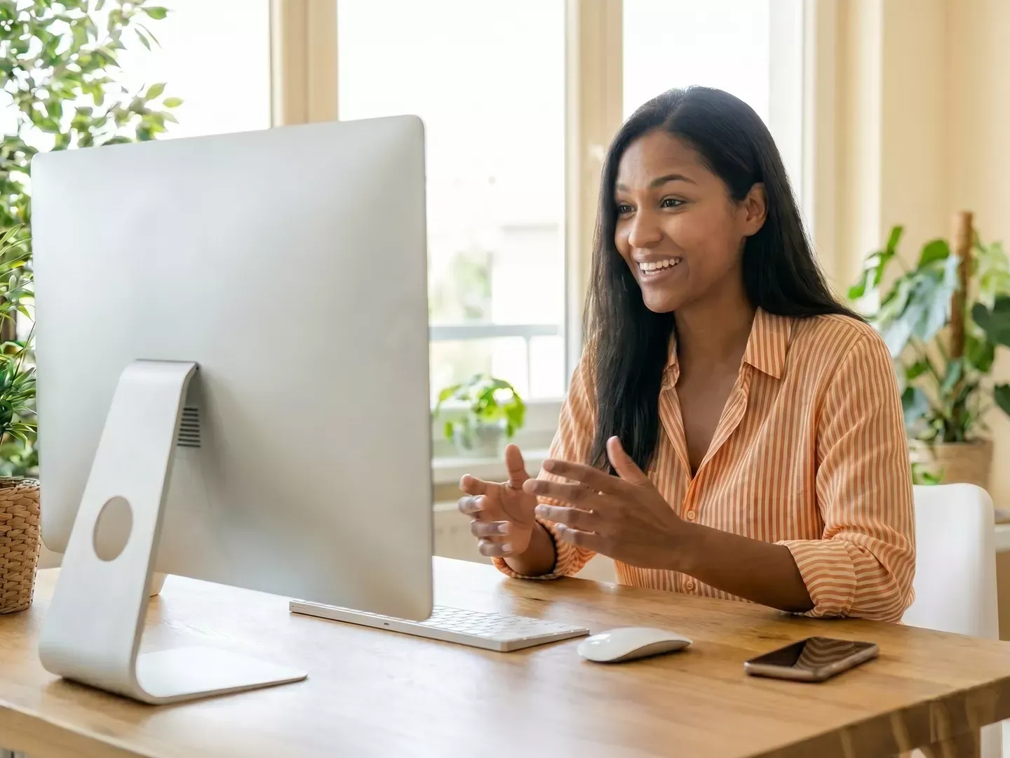 Smiling woman in orange striped blouse working from home in her home office chatting on a zoom conference call.