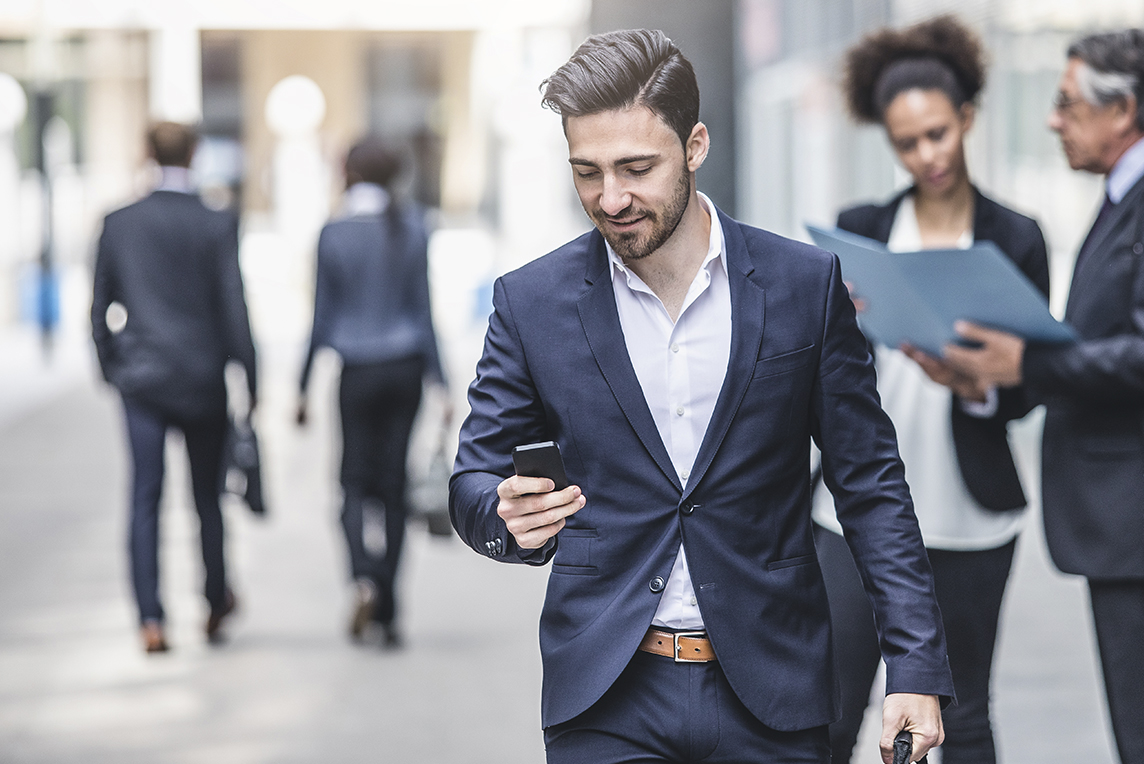 Businessman walking from office while texting on his phone