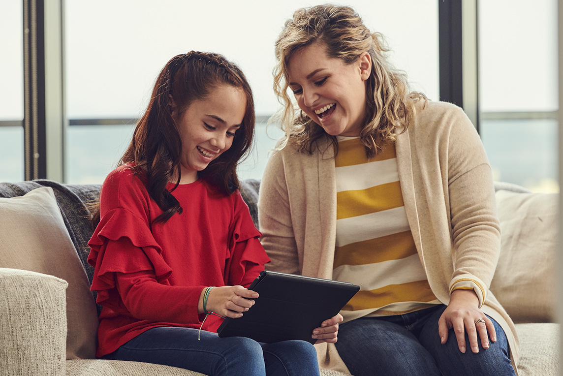 A mother and daughter sitting on the couch watching shows on the tablet