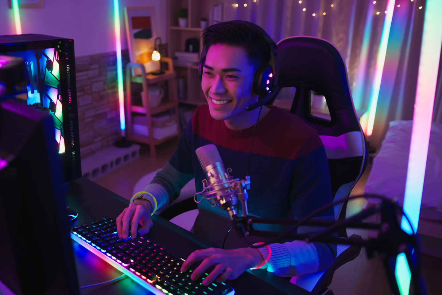Young man in a neon lit room, streaming with his fancy lit up gaming computer, headset, and streaming microphone.