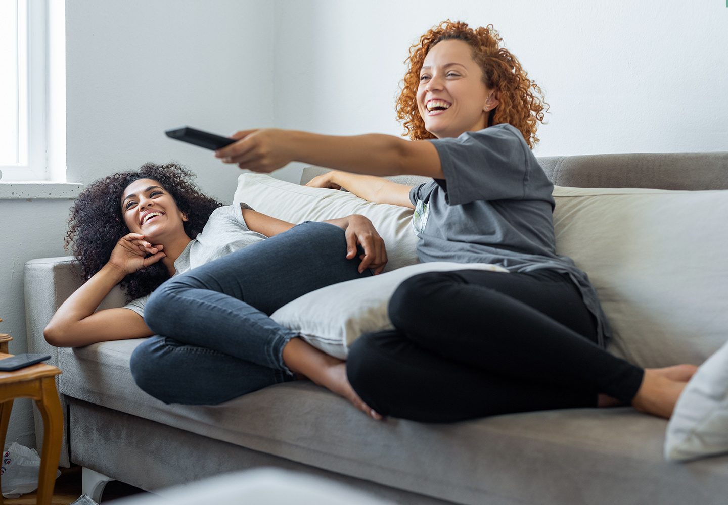 Teens laying on a sofa watching TV together