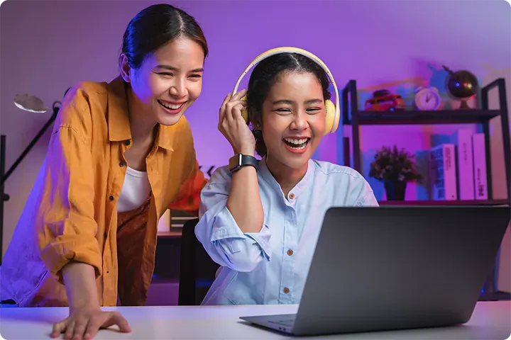 Two sisters laugh as they look at laptop.