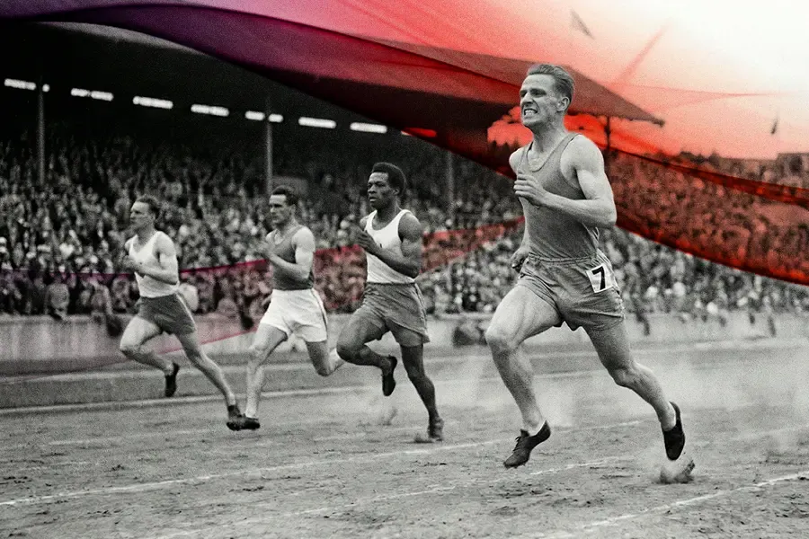 A black and white vintage-style photograph of several male runners sprinting on a dirt track in front of a crowded stadium.