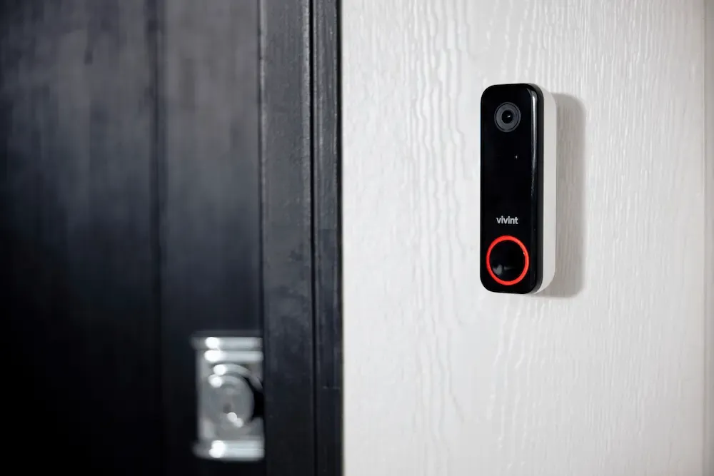 A close-up of a black Vivint Doorbell Camera Pro with a glowing red LED ring mounted on a white door frame.