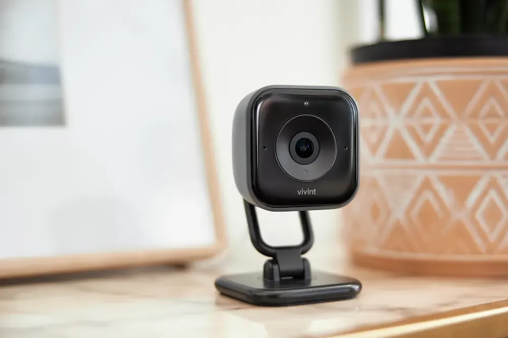 A black Vivint indoor security camera sitting on a marble surface next to a decorative terracotta pot.