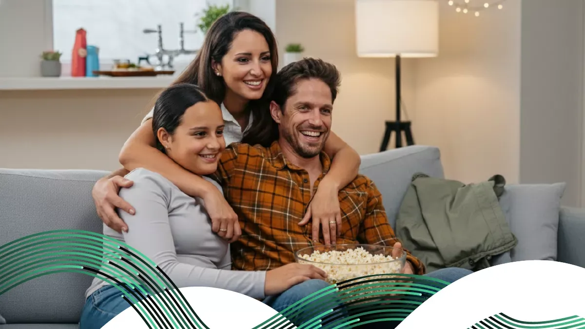 Una familia feliz de tres personas sentada en un sofá, riendo y comiendo palomitas mientras ven la televisión juntos.