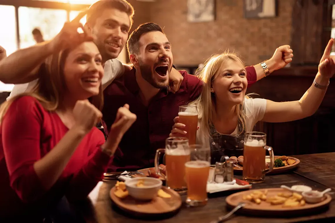 Happy people gather to watch soccer together at restaurant.