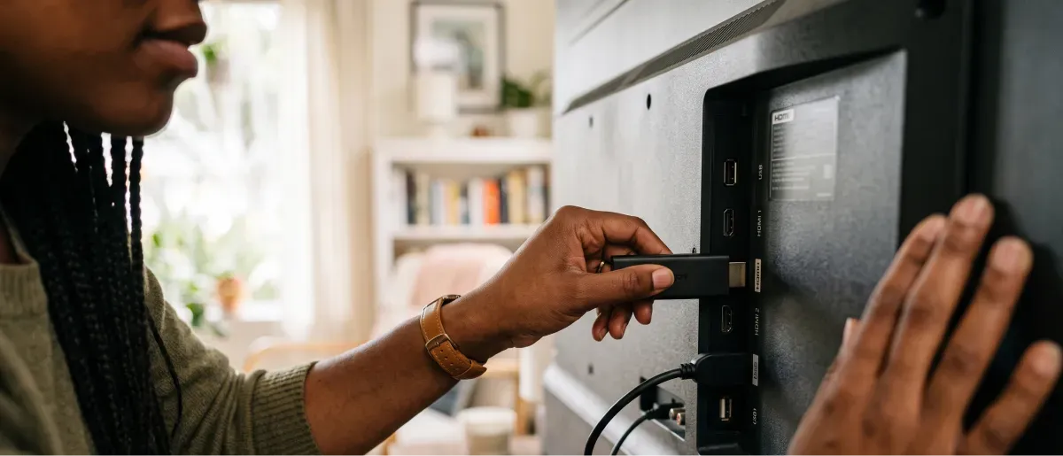 A woman plugs a streaming stick into the HDMI port on the back of a TV.