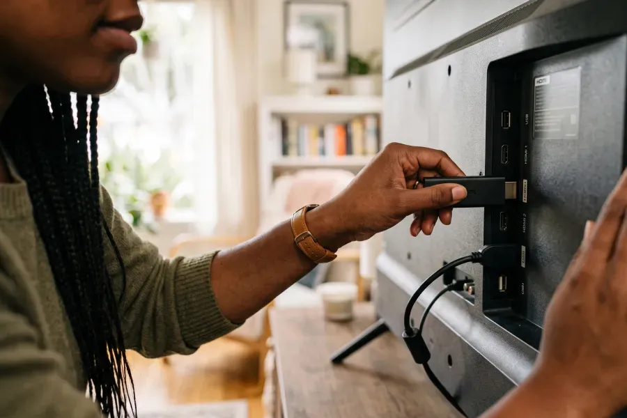 A woman plugs a streaming stick into the HDMI port on the back of a TV.