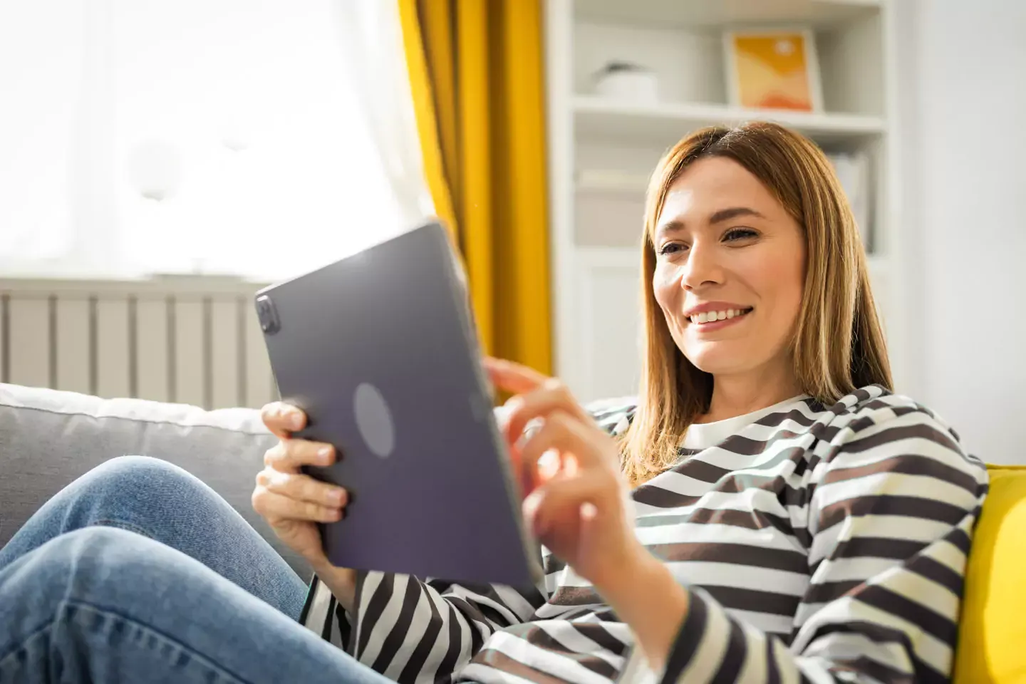 Mujer sonriente con una camisa a rayas usando una tableta.
