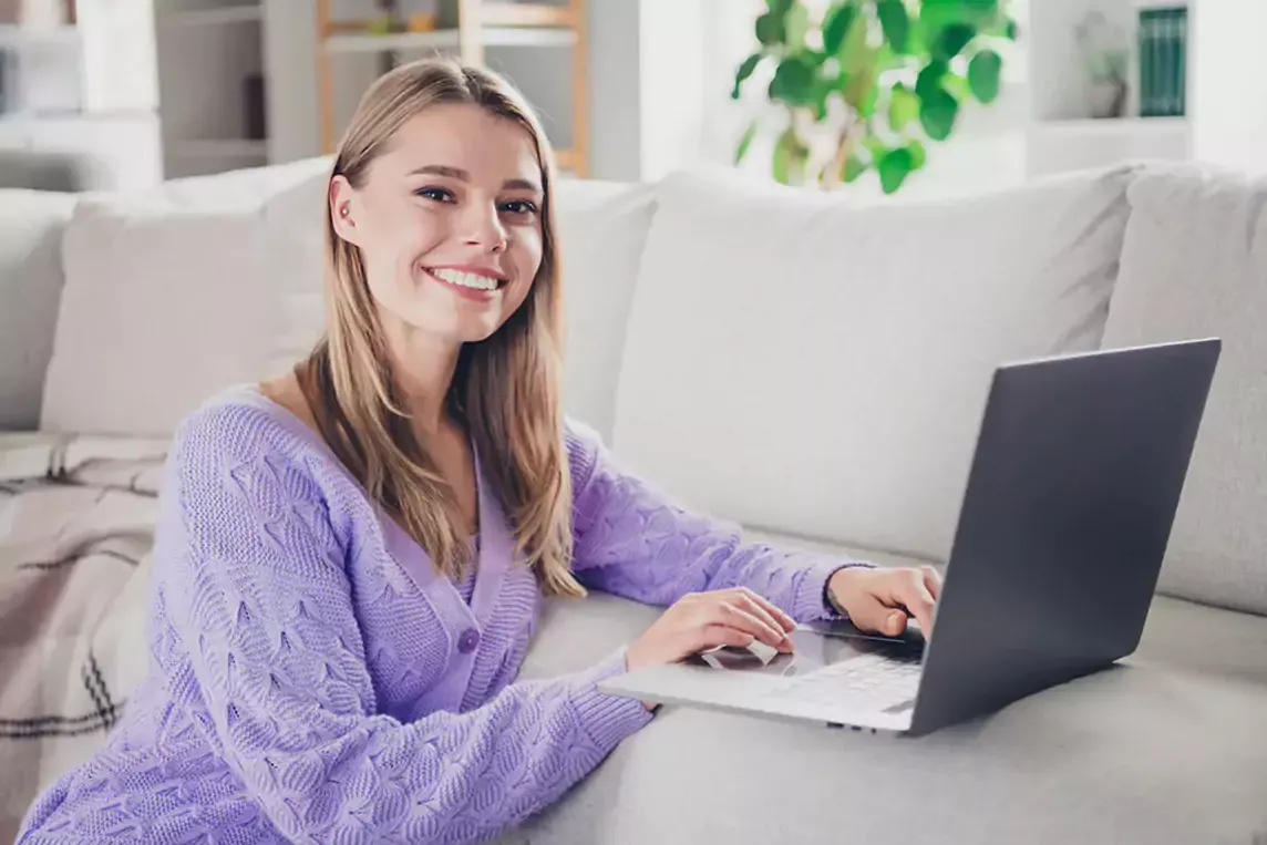 Woman uses laptop resting on couch.
