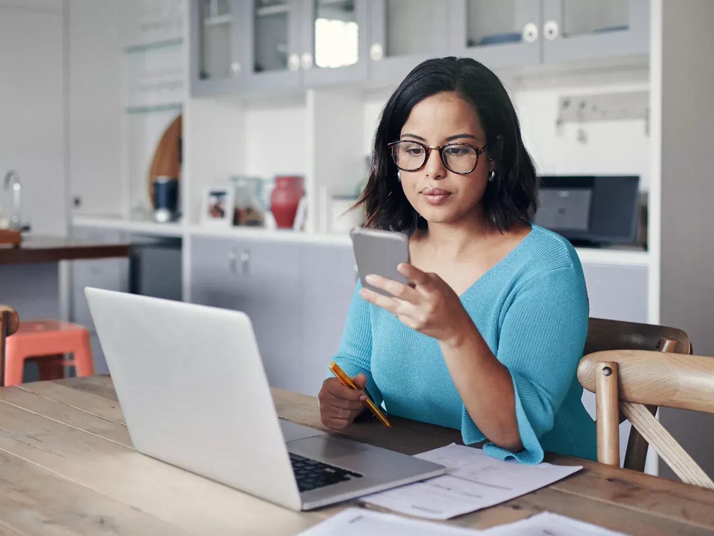 Woman sitting at her laptop and using her phone to check an app.