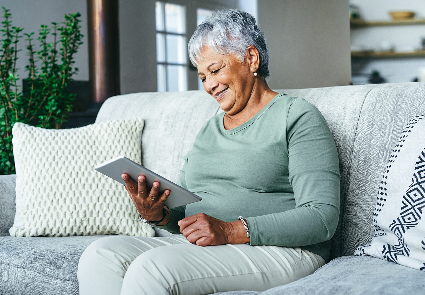 woman sitting on sofa, smiling while holding tablet